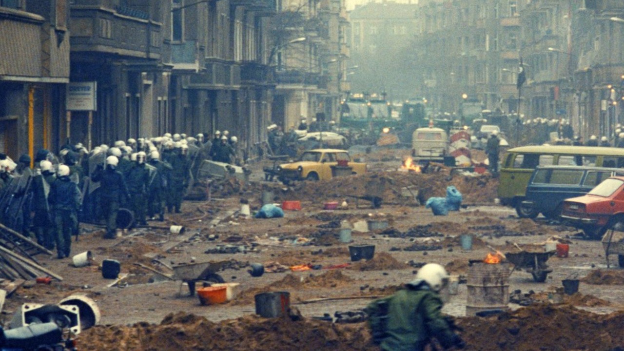 Hundreds of riot cops walk through a street that has been dug up and turned into barricades.